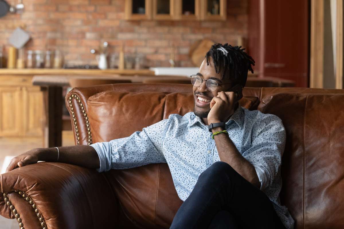 Happy thoughtful millennial Black hipster guy speaking on mobile phone (R) (S)